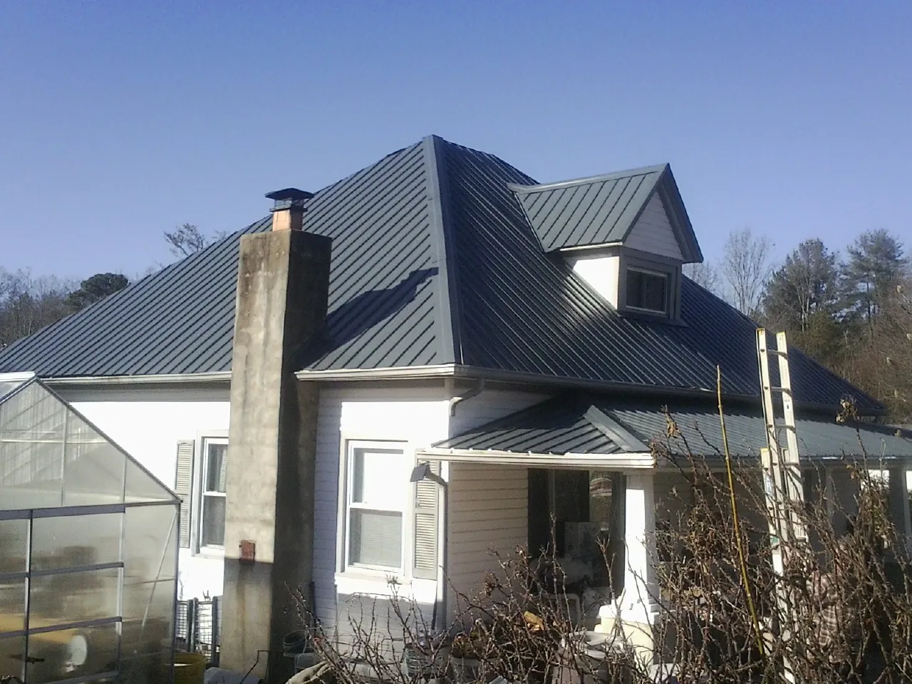 Dark blue standing seam metal roof on a white farmhouse with dormer — Slate & Tile Roof Repair by Roofing Brothers in Turner