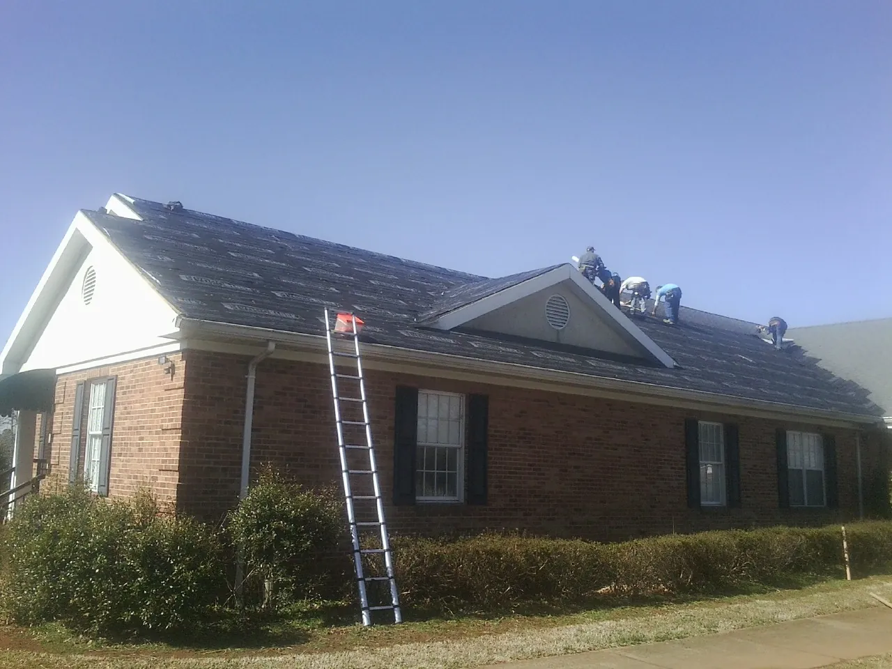 Crew tearing shingles off a brick ranch roof with a ladder set — Metal Roof Repair work by our crew in Turner