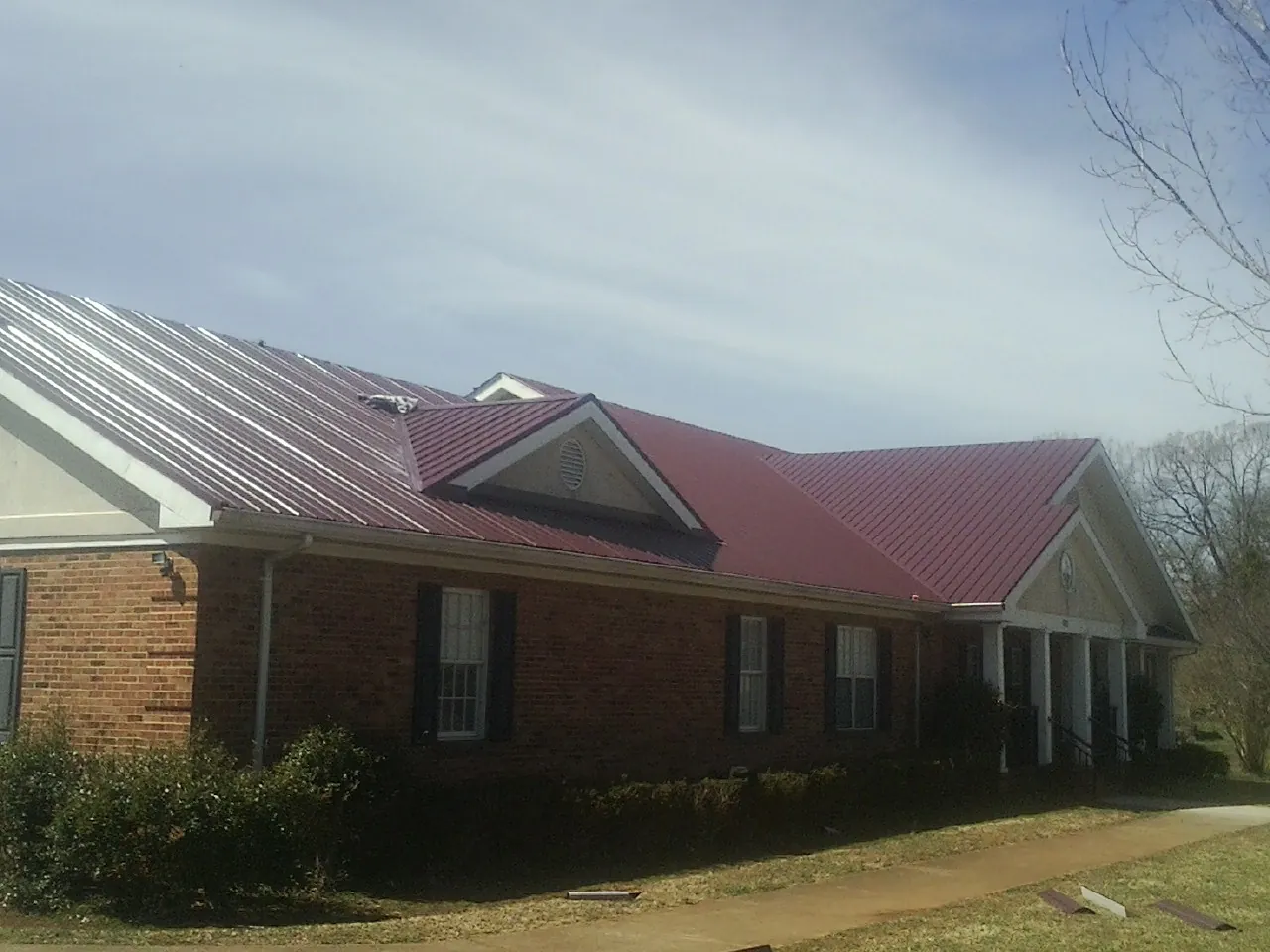 Red metal roof with gabled entries on a long brick building, from a Hail Damage Roof Repair job in Turner