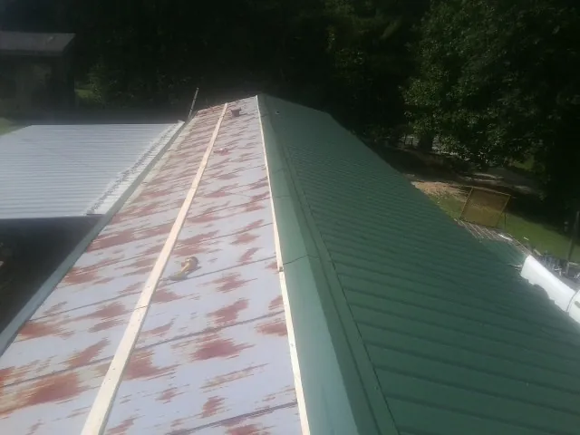 Old rusted panels beside newly installed green metal roofing — Wind Damage Roof Repair by Roofing Brothers in Turner