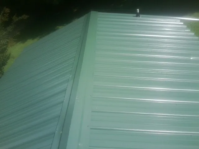 New green metal panels meeting at the ridge of a roof — Flat Roof Repair work by our crew in Turner