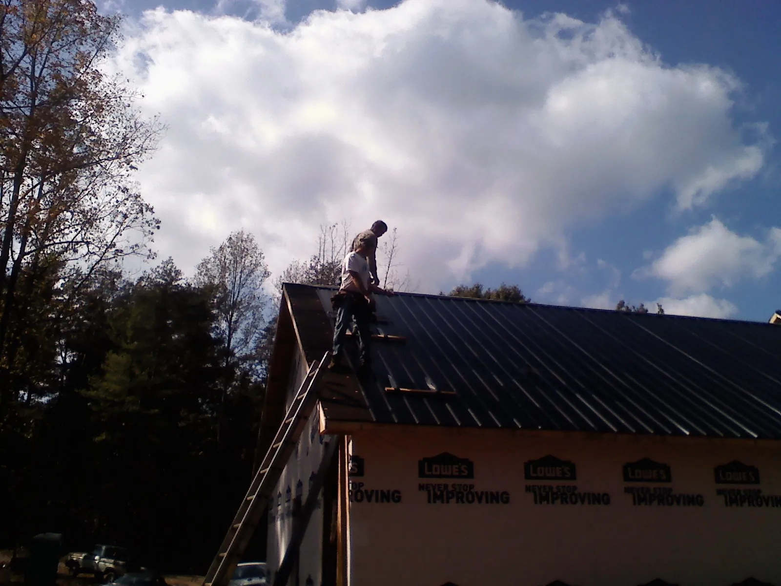 Roofer fastening dark metal panels high against a cloudy sky, from a Roof Inspection job in Turner