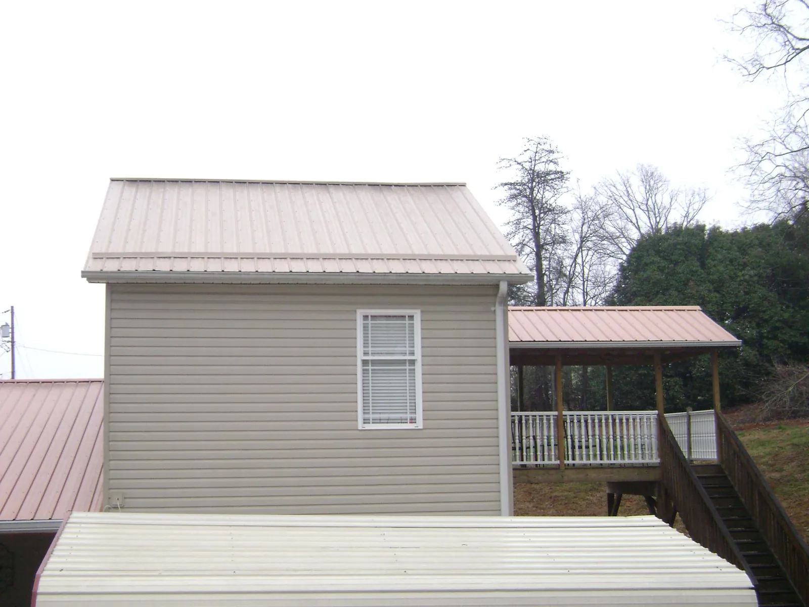 Tan metal roofs on a two story addition and attached porch, from a Roof Replacement job in Turner